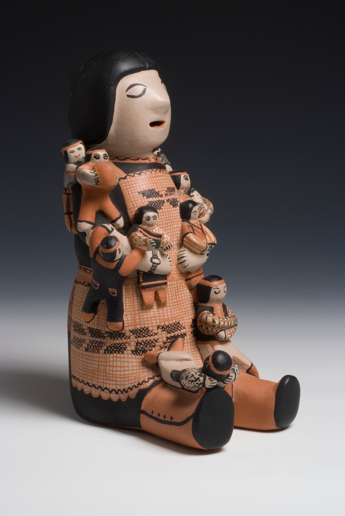 Seated pottery storyteller figure in black, cream, and orange, with small children clustered on her lap and shoulders