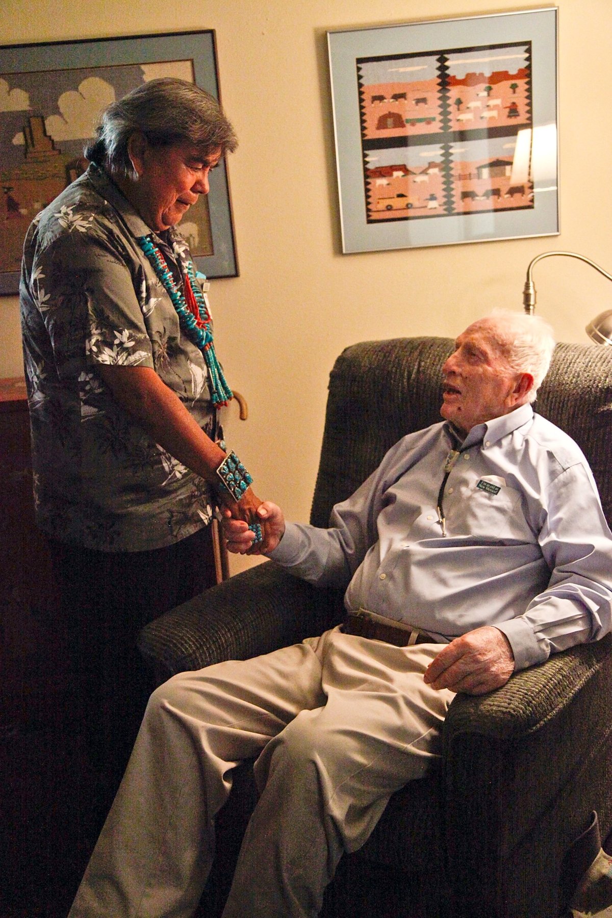 Kewa potter Robert Tenorio holding hands with John W. Kennedy, seated, in a living room hung with Navajo pictorial weavings
