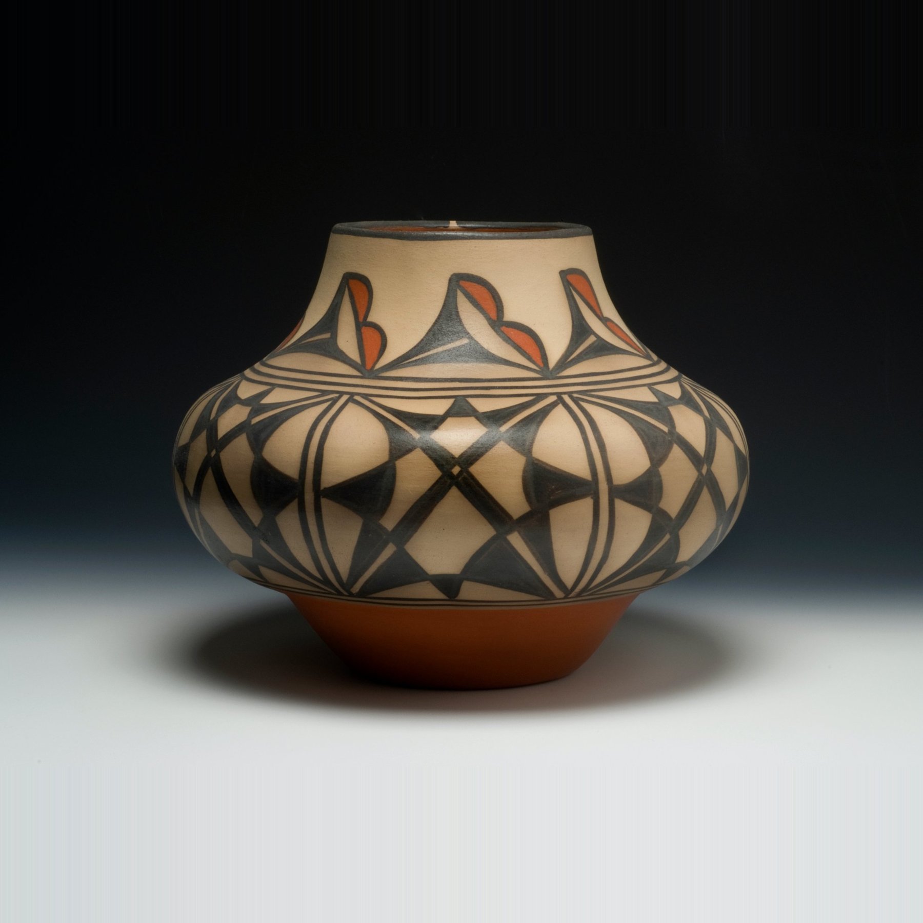 Pottery jar by Robert Tenorio with bold black geometric designs and red accents above a red base